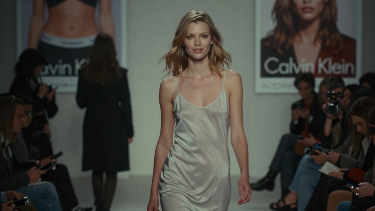 Kate Moss walking a 1990s grunge runway, pale and unsmiling, under moody lighting.
